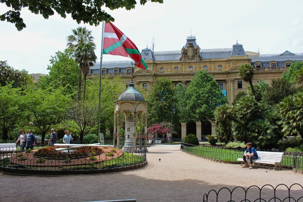 Der grüne Park der Plaza de Gipuzkoa in San Sebastián mit einer wehenden baskischen Flagge vor dem neoklassizistischen Palastgebäude der Provinzregierung.