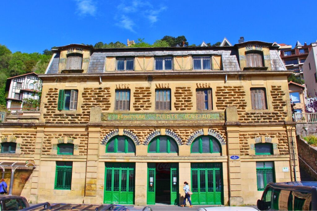 Die historische Talstation der Standseilbahn Funicular Monte Igueldo in San Sebastián, ein charmantes Jugendstilgebäude aus Stein und Fachwerk mit leuchtend grünen Holztoren.