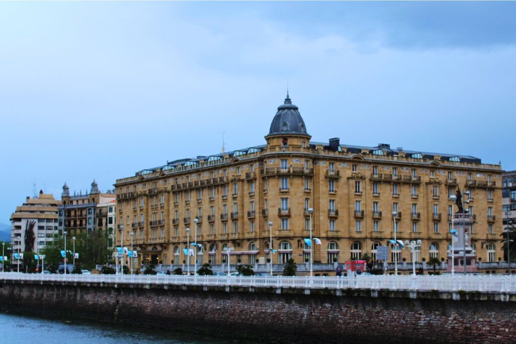 Die monumentale Belle-Époque-Fassade des luxuriösen Hotel Maria Cristina in San Sebastián am Ufer des Flusses Urumea unter bewölktem Himmel.