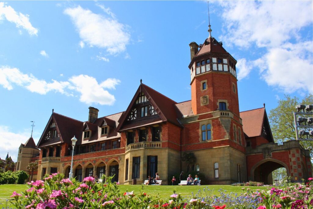 Der Palacio de Miramar in San Sebastián, eine königliche Sommerresidenz aus rotem Backstein im englischen Landhausstil, umgeben von einer grünen Wiese mit bunten Blumen.