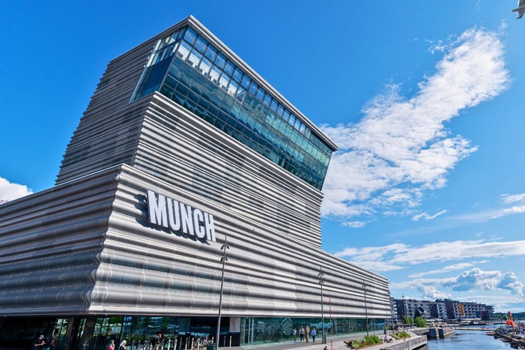 Das markante, graue Hochhaus des neuen Munch Museums (MUNCH) mit seiner geknickten Spitze und dem großen weißen Schriftzug an der Fassade unter blauem Himmel.