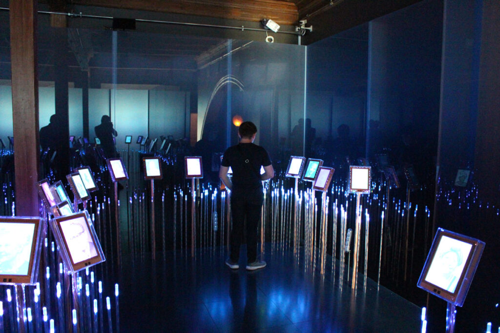 Ein abgedunkelter Raum im Nobel-Friedenszentrum, in dem hunderte kleine Bildschirme auf dünnen Stielen wie leuchtende Blumen stehen und blaues Licht ausstrahlen ("Nobel Field").