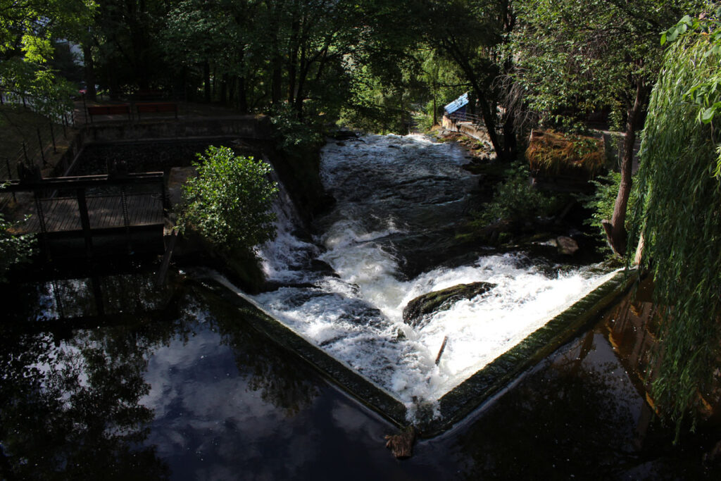 Blick von oben auf die schäumenden, wilden Wassermassen des Mølla-Wasserfalls in Oslo, die über ein Wehr fließen, eingerahmt von dichten grünen Bäumen.