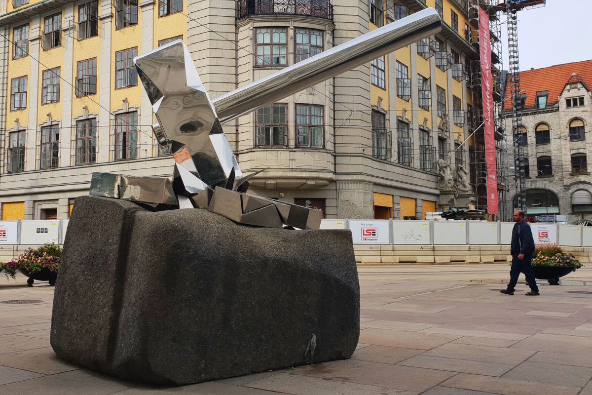 Die Skulptur "Knus nazismen" (Zerschlagt den Nazismus) vor dem Osloer Hauptbahnhof: Ein riesiger, glänzender Hammer zerschmettert ein Hakenkreuz auf einem massiven Steinblock.