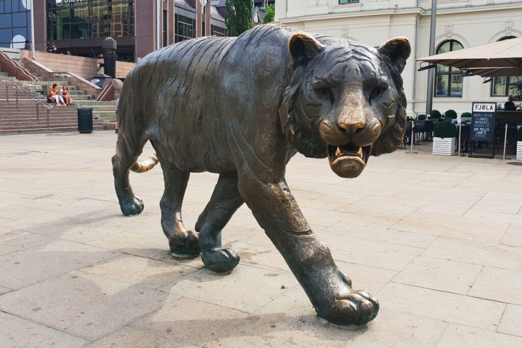 Die riesige bronzene Tiger-Statue ("Tigeren") auf dem Jernbanetorget vor dem Osloer Hauptbahnhof. Der Tiger schreitet dynamisch mit geöffnetem Maul auf den Betrachter zu.