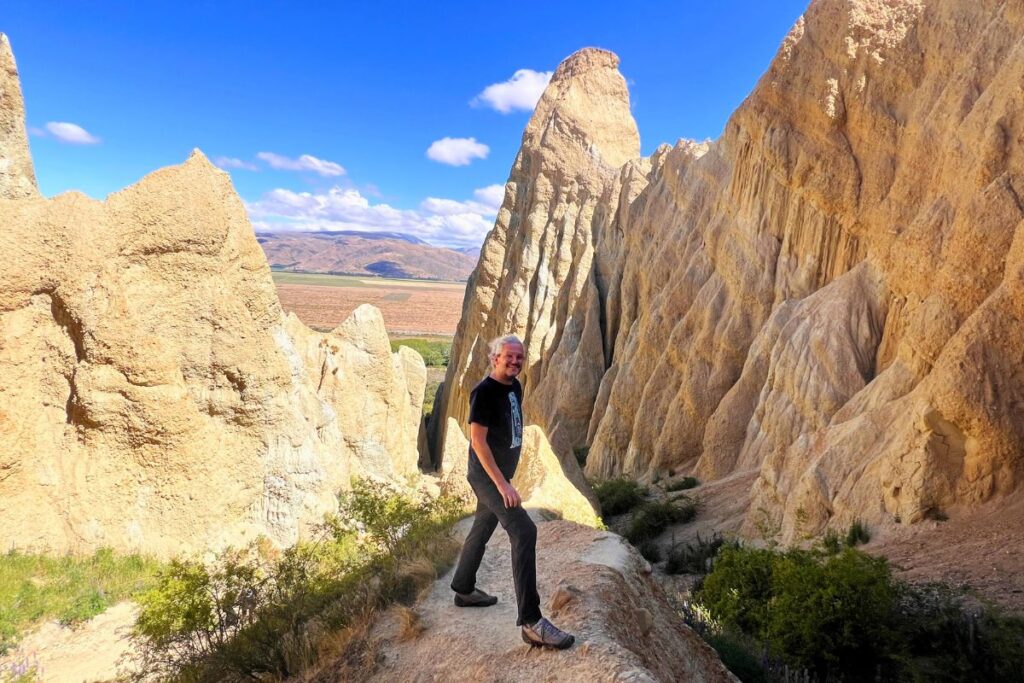 Reiseblogger Nicolo Martin steht auf einem schmalen Grat inmitten der riesigen, zerklüfteten Lehmformationen der Clay Cliffs bei Omarama.