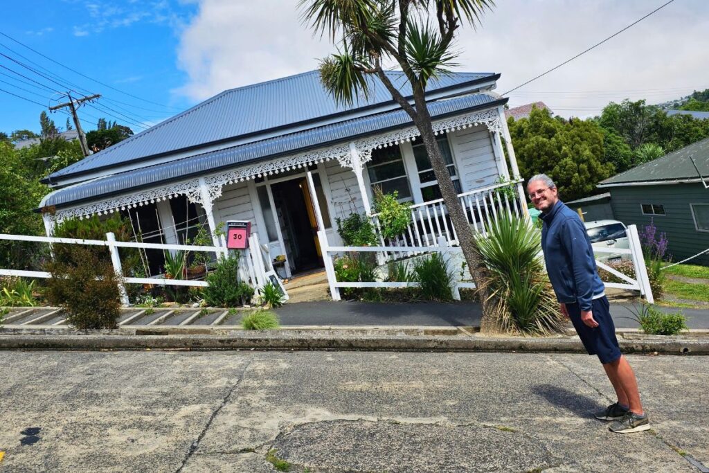 Reiseblogger Nicolo steht in extremer Schräglage auf der Baldwin Street in Dunedin, um die Steigung der steilsten Straße der Welt zu demonstrieren.