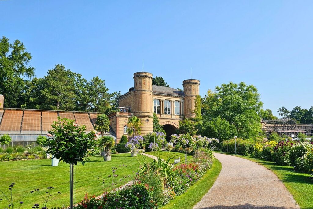 Eingangstor des Botanischen Gartens Karlsruhe mit Türmen, Blumenrabatten und Spazierweg