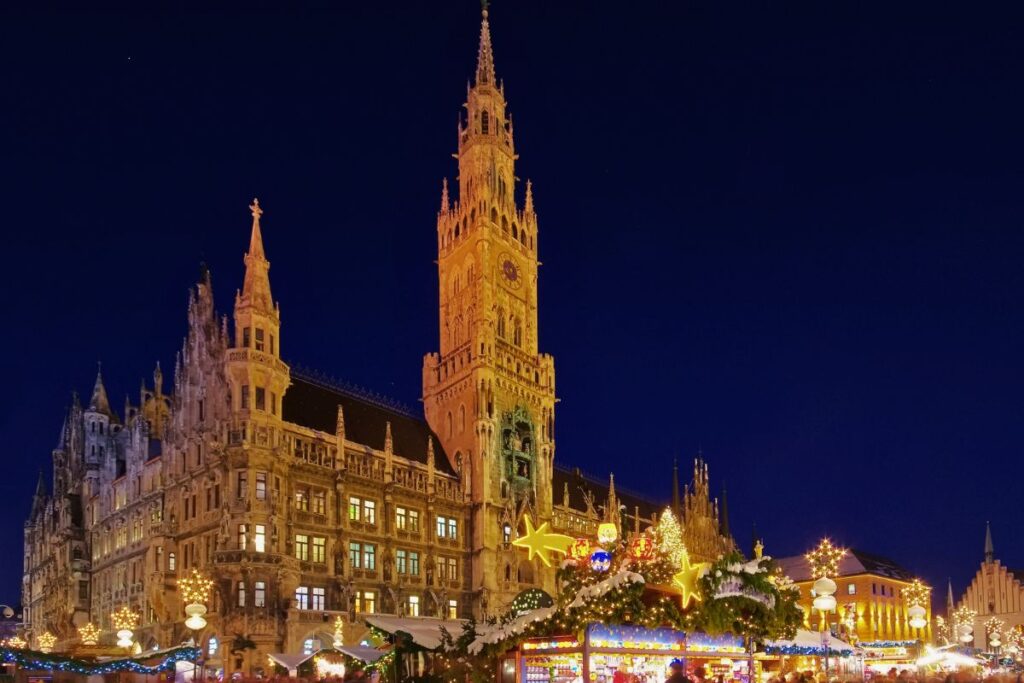 Der hell erleuchtete Münchner Christkindlmarkt auf dem Marienplatz vor dem neugotischen Rathaus bei Nacht.