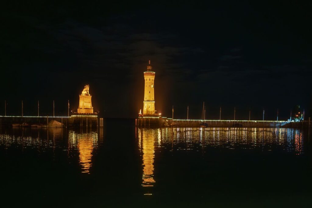 Die beleuchtete Hafeneinfahrt von Lindau am Bodensee mit bayerischem Löwen und Leuchtturm bei Nacht.