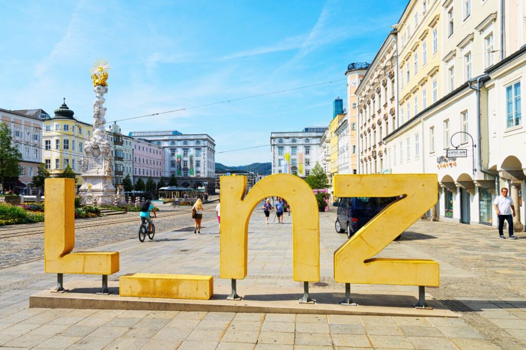 Linz-Schriftzug am Hauptplatz mit barocken Gebäuden und Dreifaltigkeitssäule