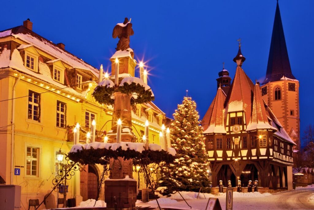 Verschneiter Weihnachtsmarkt in Michelstadt mit dem historischen Rathaus auf Stelzen, Holzfiguren und Weihnachtsbaum.