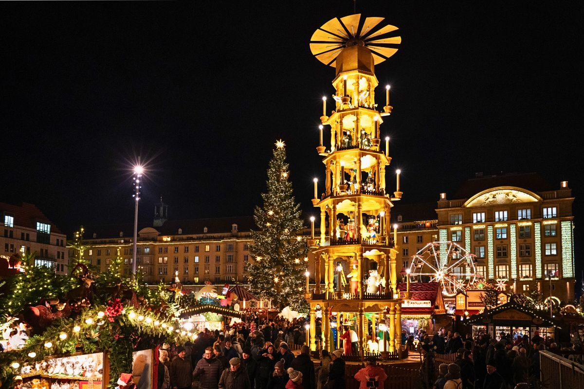 Stimmungsvolle Nachtaufnahme des Dresdner Striezelmarktes mit der weltgrößten erzgebirgischen Stufenpyramide, einem großen Weihnachtsbaum und vielen Besuchern. Das Titelbild für den Reiseführer zu den schönsten Weihnachtsmärkten in Sachsen.