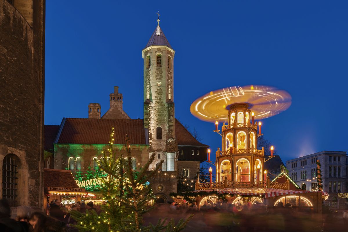 Der Braunschweiger Weihnachtsmarkt auf dem historischen Burgplatz mit beleuchteter Holzpyramide und dem Dom St. Blasii im Hintergrund.