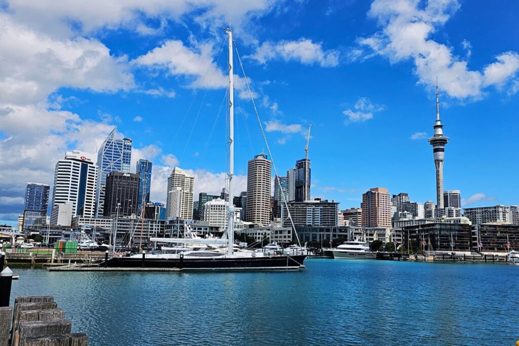 Panoramablick auf die Skyline von Auckland mit dem Sky Tower und Segelbooten im Viaduct Harbor unter blauem Himmel.