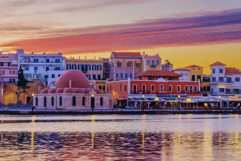 Der venezianische Hafen von Chania auf Kreta bei einem farbenfrohen Sonnenuntergang mit der markanten rosa Kuppel der Janitscharen-Moschee.