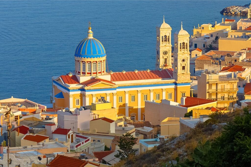 Blick über die hellen Dächer von Ermoupolis auf Syros mit der imposanten Kirche St. Nicholas und ihrer blauen Kuppel vor dem tiefblauen Meer.