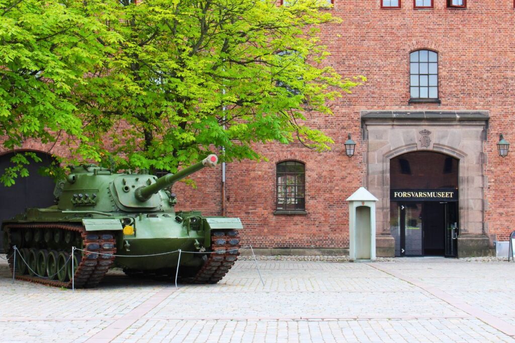 Eingang des Forsvarsmuseet in Oslo mit einem grünen Panzer unter einem Baum vor dem Backsteingebäude