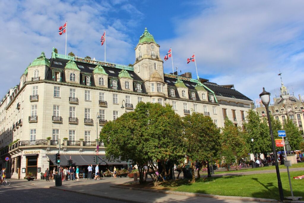 Das historische Grand Hotel in Oslo mit grünem Turmdach und norwegischen Flaggen, gesehen vom Eidsvolls plass