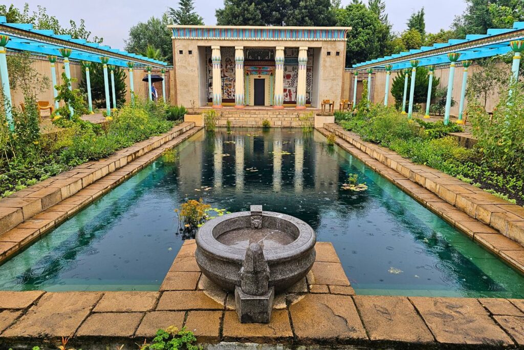 Der ägyptische Garten in den Hamilton Gardens mit einem rechteckigen Wasserbecken und bemalten Säulen unter bewölktem Himmel.