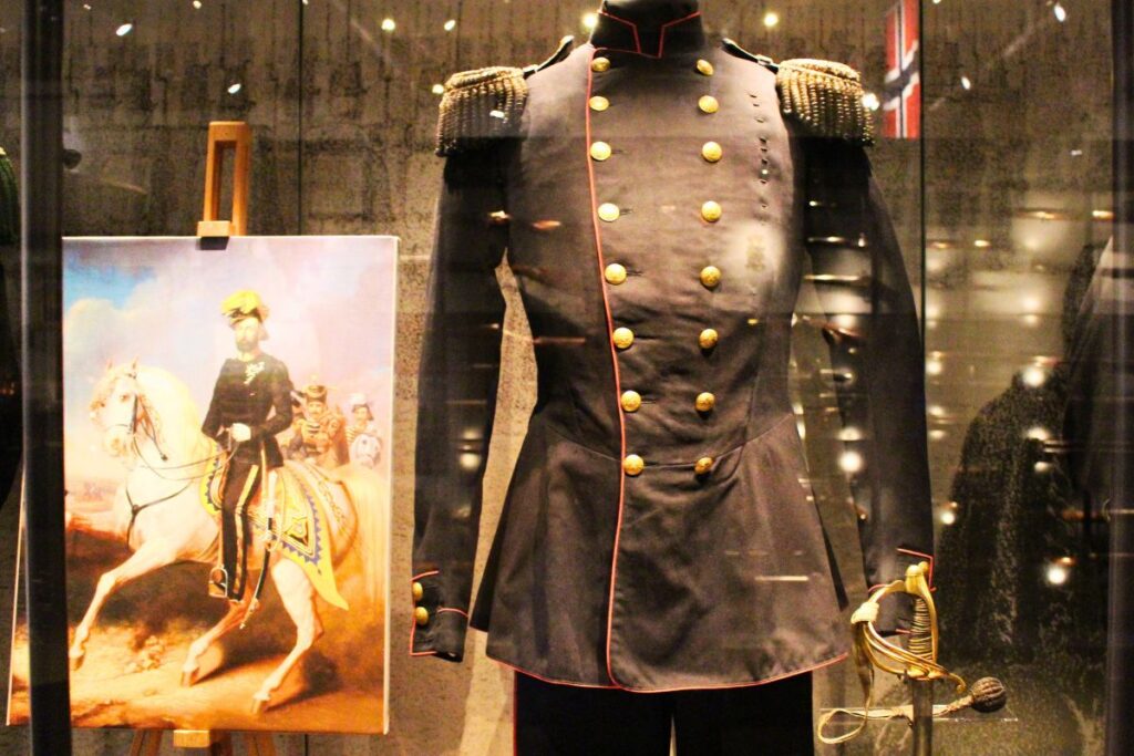 Historische schwarze Militäruniform mit goldenen Knöpfen und Epauletten neben einem Gemälde eines Reiters in einer Vitrine