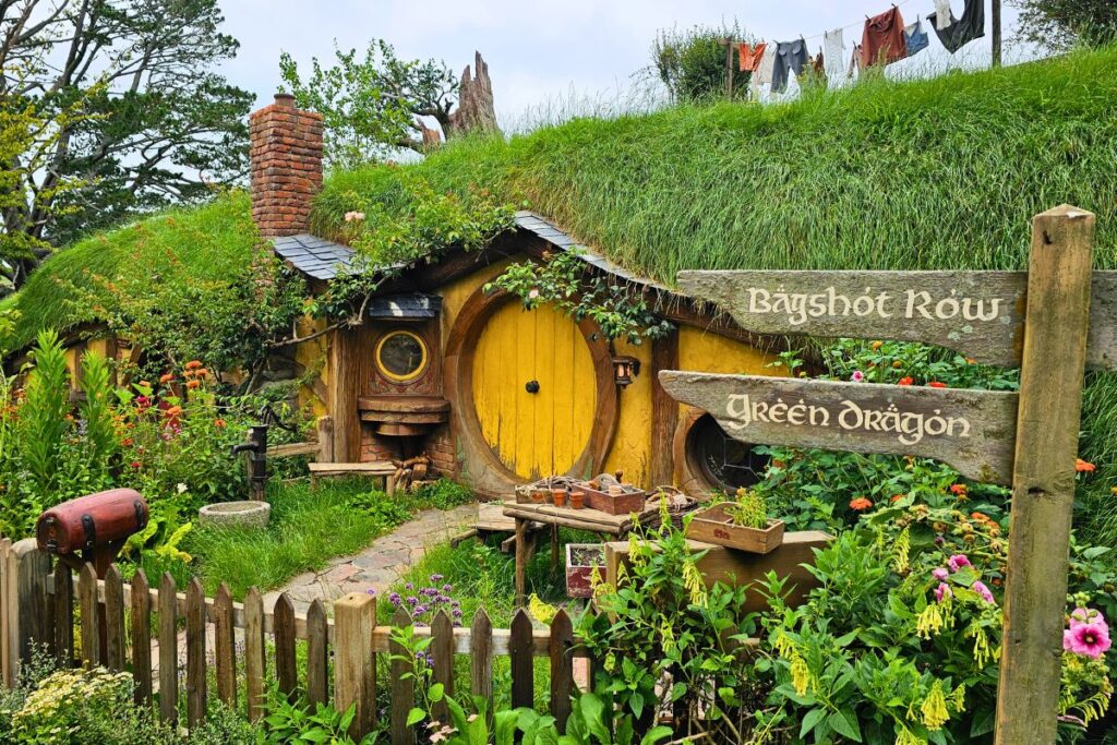 Eine gelbe Hobbithöhle mit runder Tür und üppigem Blumengarten im Hobbiton Movie Set in Matamata.
