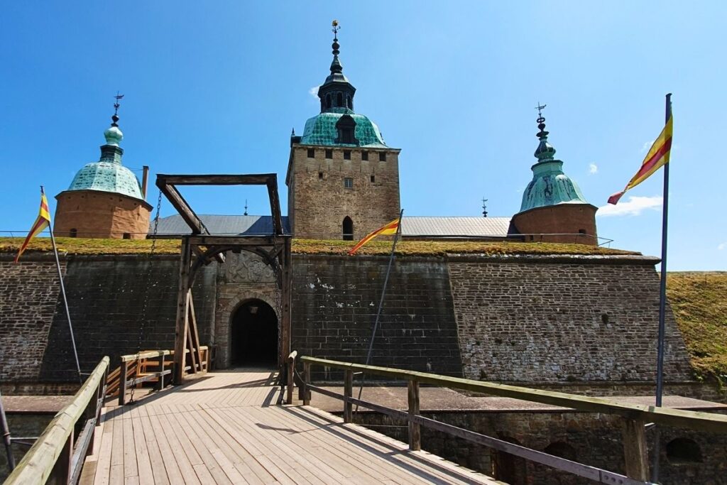 Die massiven Mauern und Türme von Schloss Kalmar mit der hölzernen Zugbrücke vor strahlend blauem Himmel.