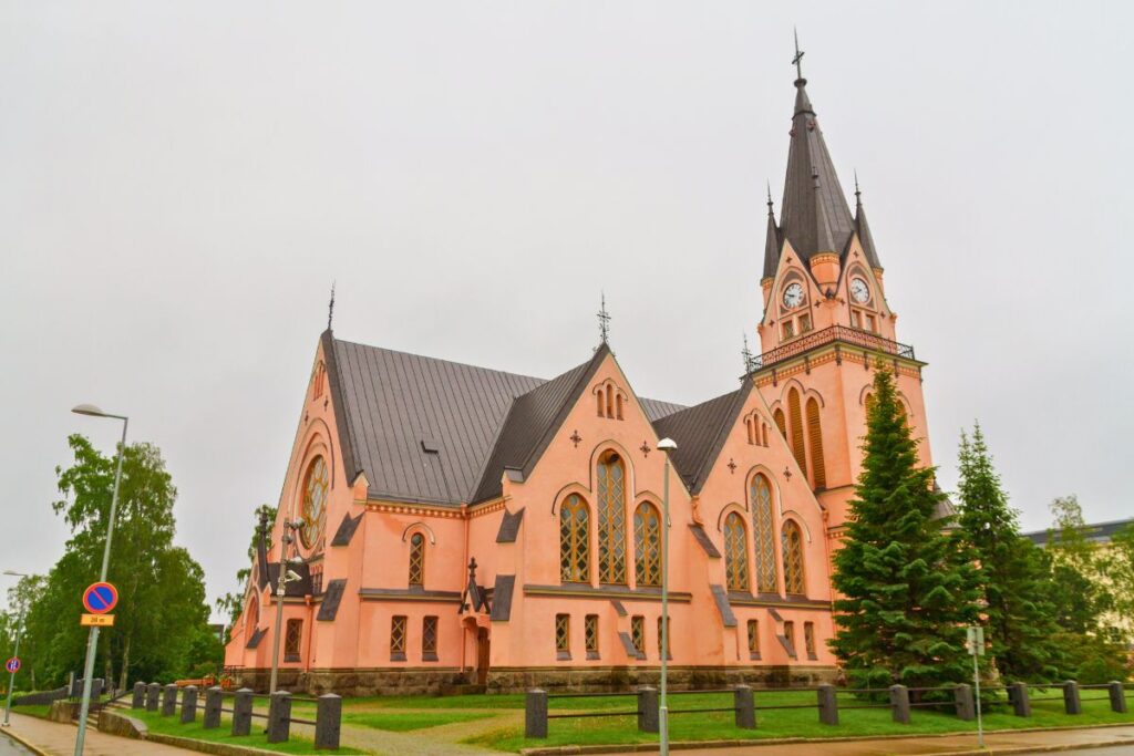 Die leuchtend rosafarbene neogotische Kirche von Kemi mit hohem Turm an einem bewölkten Tag.