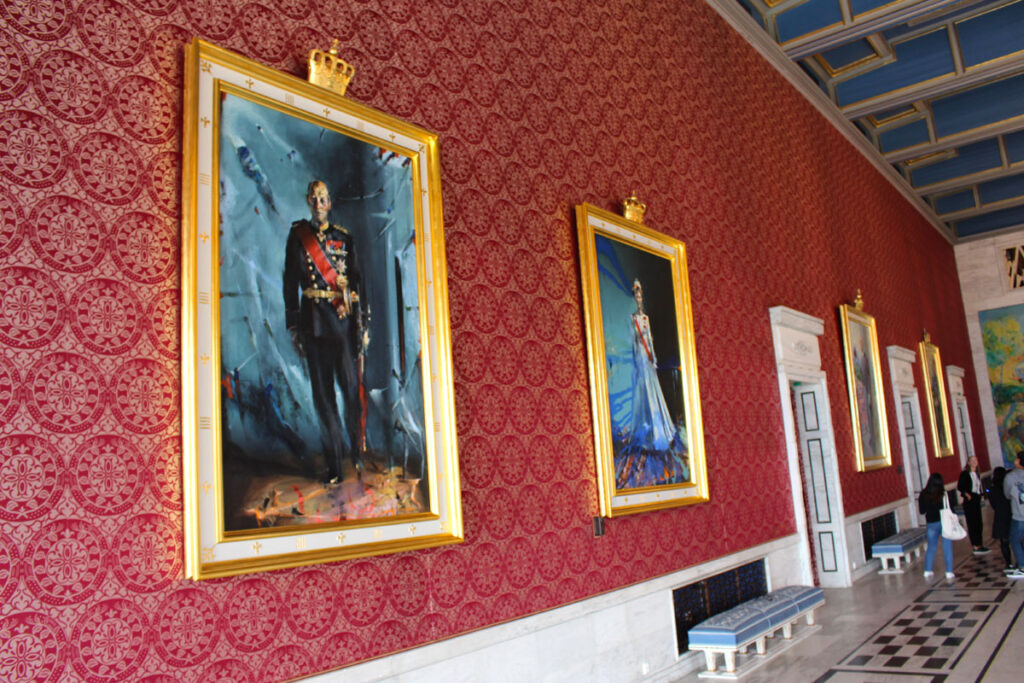 Offizielle Porträts von König Harald V. und Königin Sonja hängen in goldenen Rahmen an einer roten Wand im Osloer Rathaus