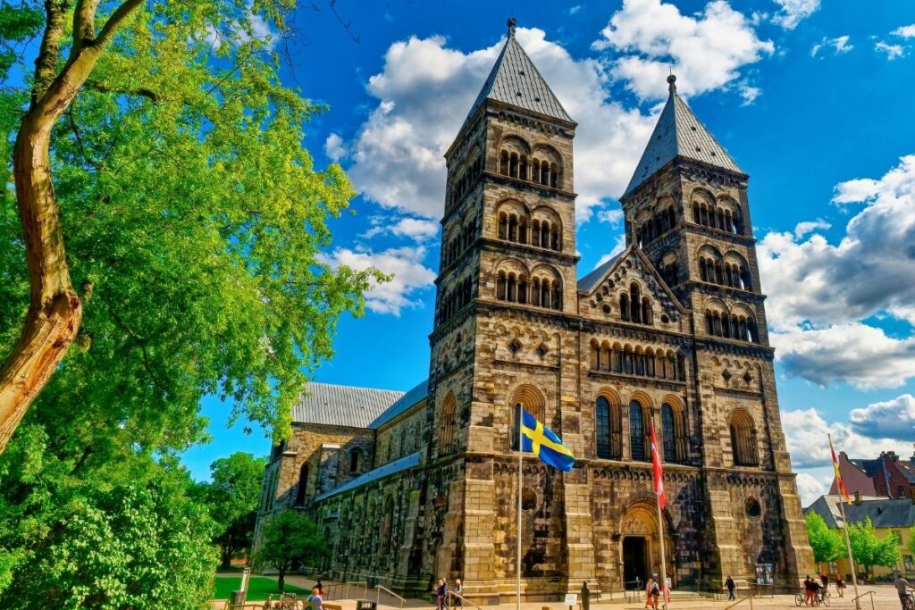 Die imposante Frontfassade des Doms zu Lund mit ihren zwei Türmen im romanischen Stil, davor weht die schwedische Flagge.