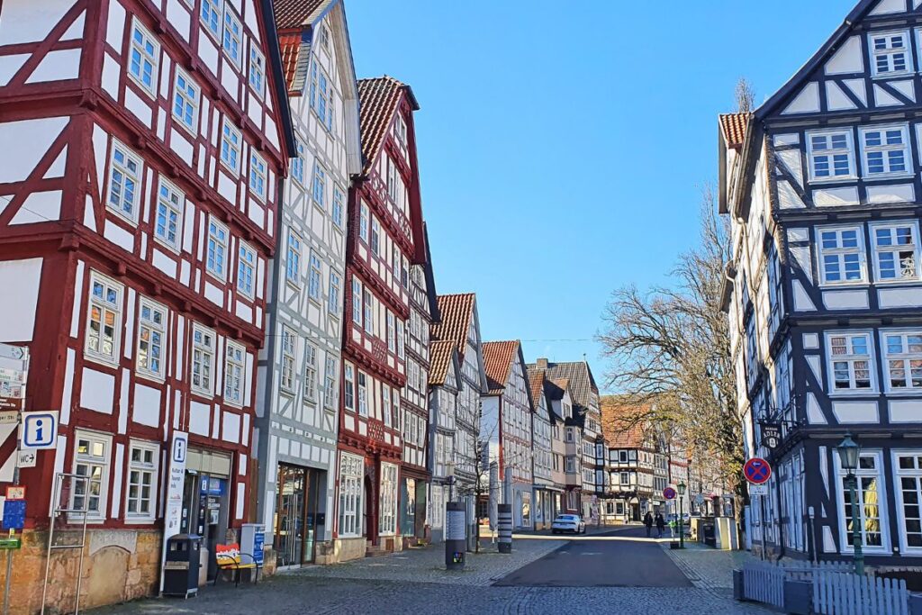 Blick in eine weite Gasse der Melsunger Altstadt mit einer geschlossenen Reihe prachtvoller Fachwerkhäuser und Kopfsteinpflaster unter blauem Himmel.