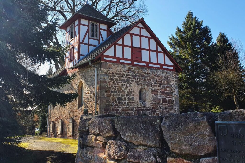 Die kleine Hospitalskapelle St. Georg in Melsungen mit ihren massiven Steinmauern und dem markanten Fachwerk-Giebel im Sonnenlicht.