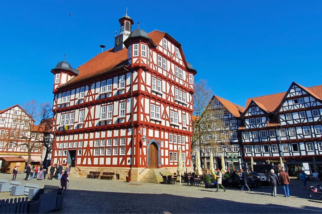 Das berühmte Melsunger Rathaus, ein freistehender Fachwerkbau mit Ecktürmen, auf dem sonnigen Marktplatz unter strahlend blauem Himmel.