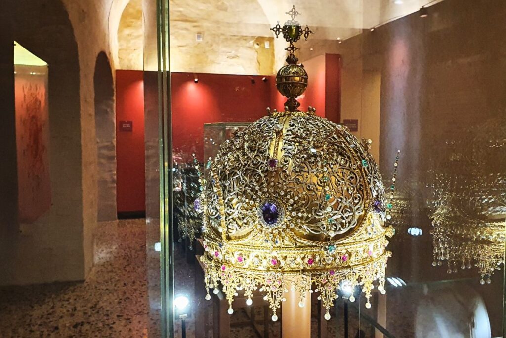 Eine prunkvolle, goldene Krone mit Edelsteinen in einer Glasvitrine im Schmuckmuseum von Vicenza.