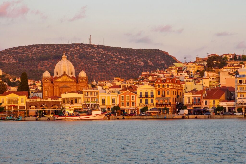 Die Uferpromenade von Mytilene auf der Insel Lesbos bei Sonnenuntergang, dominiert von der großen, beleuchteten Kuppel der Kirche Agios Therapon.