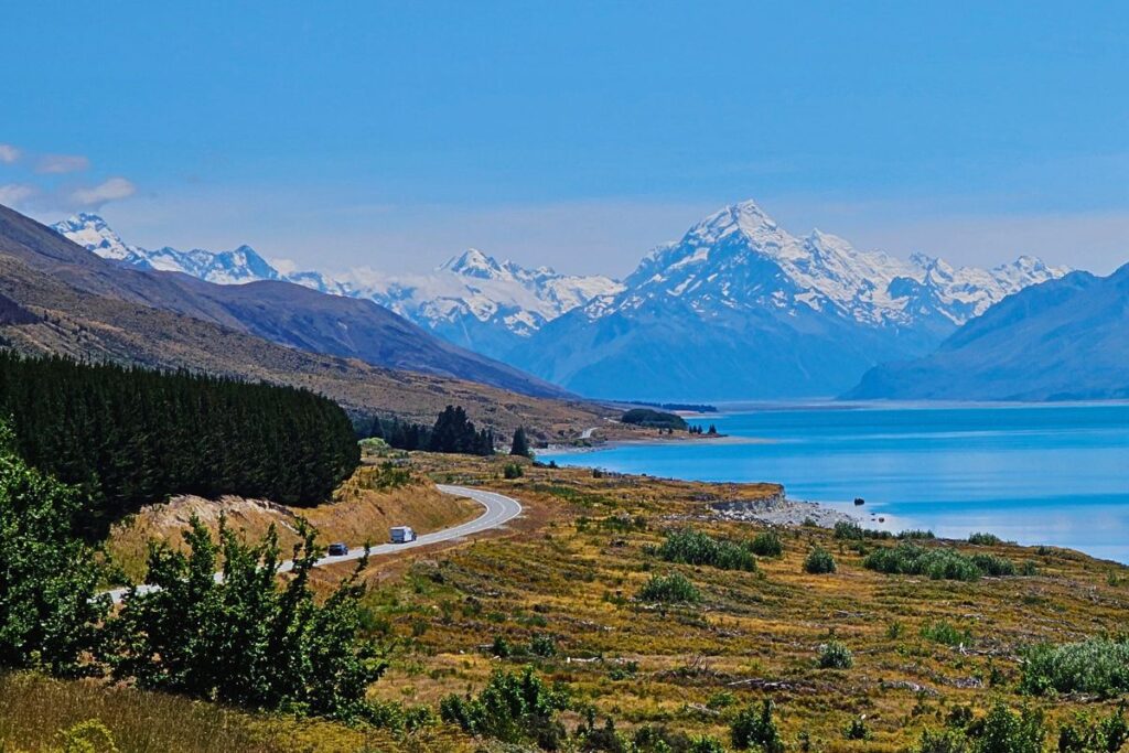 Blick über den türkisblauen Lake Pukaki auf die schneebedeckten Gipfel der Neuseeländischen Alpen mit dem Mount Cook (Aoraki) im Zentrum.