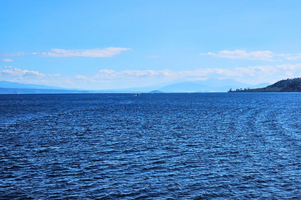 Weite Sicht über das tiefe Blau des Lake Taupō auf der Nordinsel Neuseelands, am Horizont zeichnen sich die Vulkane des Tongariro Nationalparks ab.