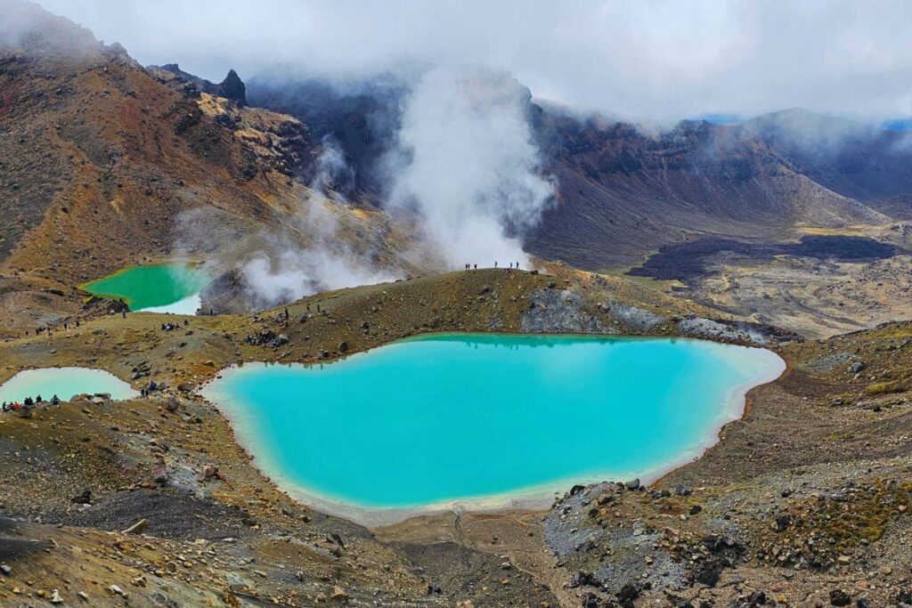 Blick von oben auf die leuchtend türkisfarbenen Emerald Lakes im Tongariro Nationalpark mit aufsteigendem Dampf aus Schwefelquellen.