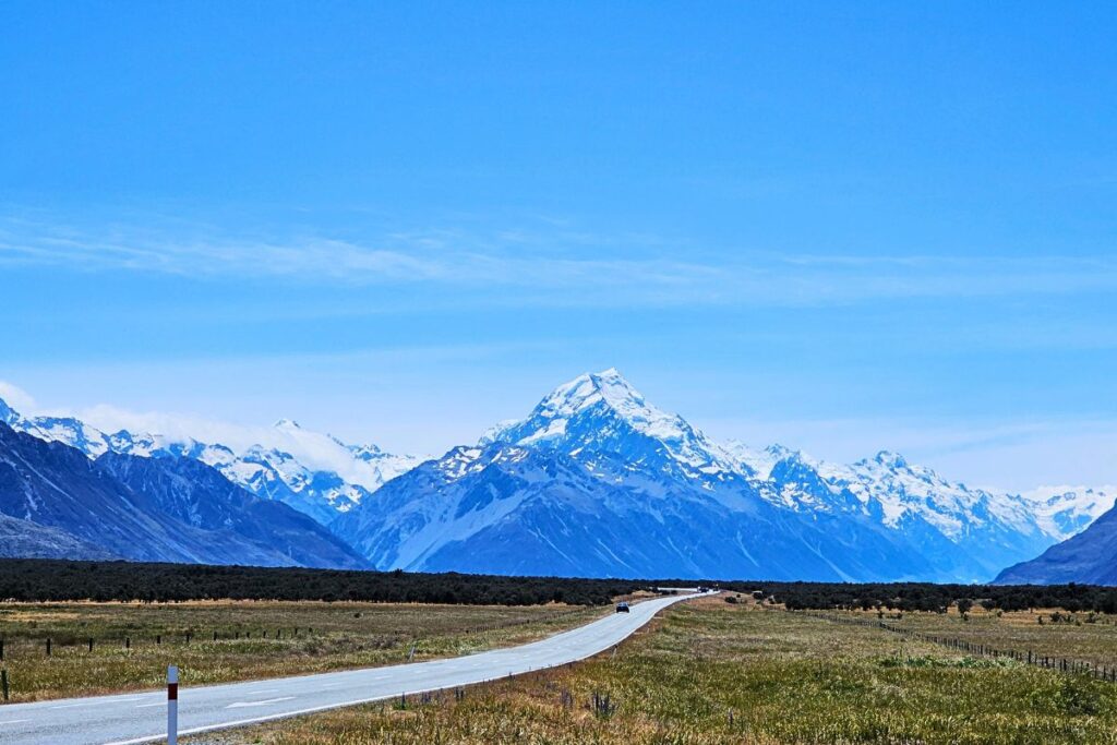 Die lange, gerade Straße führt direkt auf den majestätischen, schneebedeckten Gipfel des Mount Cook (Aoraki) zu.