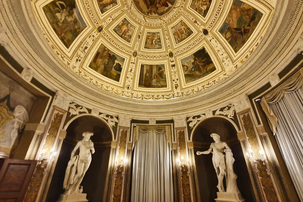Blick nach oben in eine prachtvolle Kuppel im Palazzo Thiene mit mythologischen Fresken in Kassettenfeldern, darunter weiße klassische Statuen in Wandnischen.