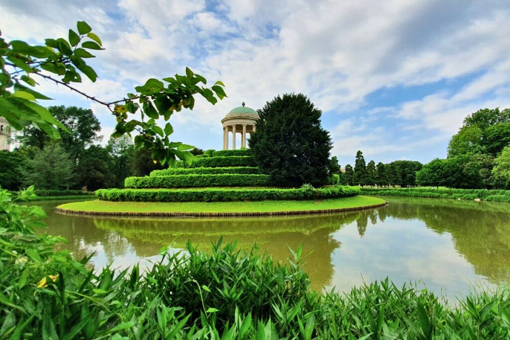 Ein kleiner Rundtempel auf einem grünen Hügel mitten im Parco Querini in Vicenza, davor ein ruhiger See.