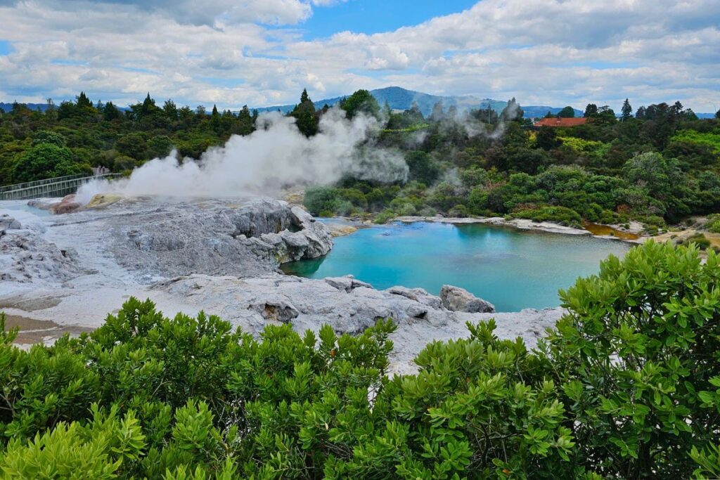 Der Pohutu Geysir im Te Puia Valley in Rotorua schießt eine hohe weiße Wasserfontäne in den bewölkten Himmel.