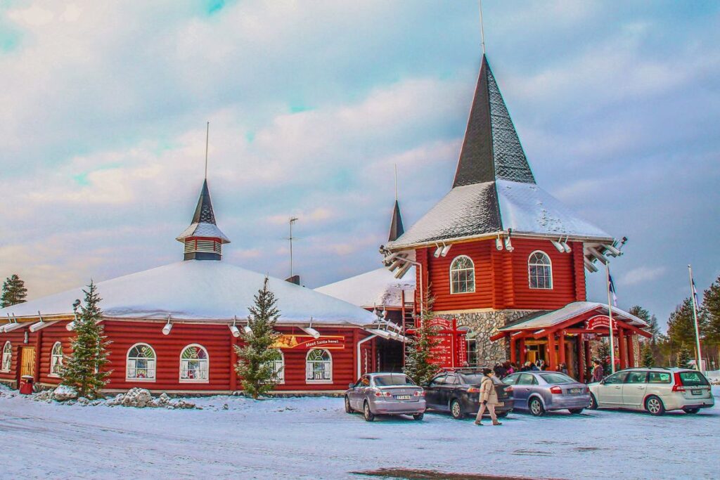 Das verschneite Santa Claus Village in Rovaniemi mit festlicher Beleuchtung und markanten roten Gebäuden.