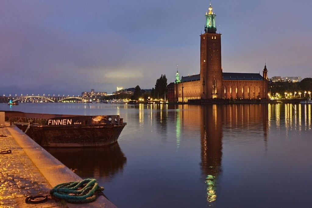 Das beleuchtete Stockholmer Rathaus (Stadshuset) mit seinem markanten Turm spiegelt sich zur blauen Stunde im Wasser des Mälarsees.