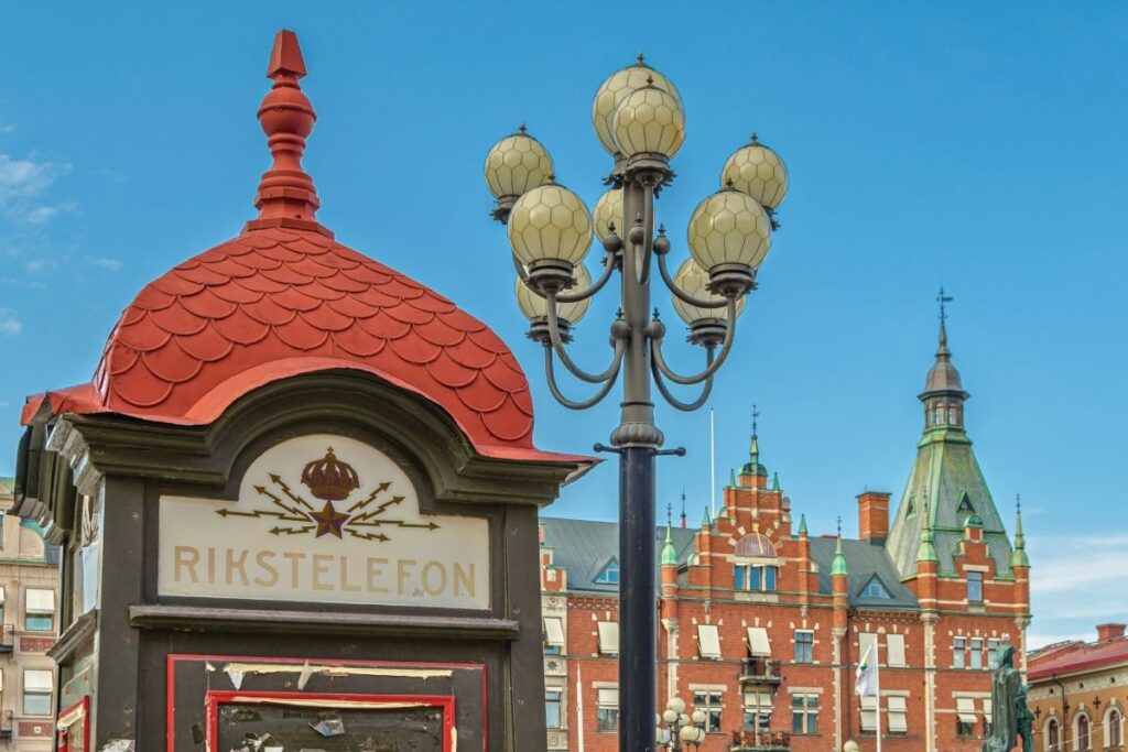 Eine historische schwedische Telefonzelle ("Rikstelefon") auf dem Marktplatz von Sundsvall, im Hintergrund prächtige Steingebäude.