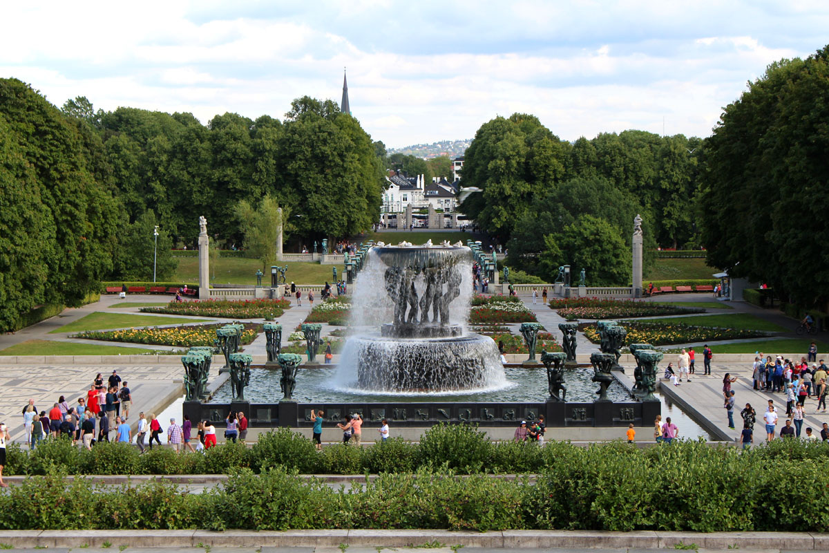 Weitblick über die gepflegten Blumenbeete und Wege des Vigeland Parks in Oslo mit dem Brunnen im Hintergrund und vielen Besuchern