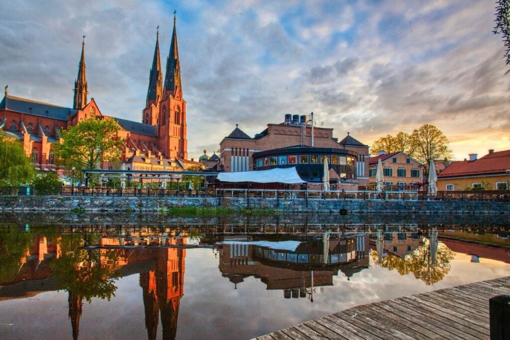Die beeindruckende Kathedrale von Uppsala und historische Gebäude spiegeln sich bei Sonnenuntergang im ruhigen Wasser des Flusses Fyrisån.
