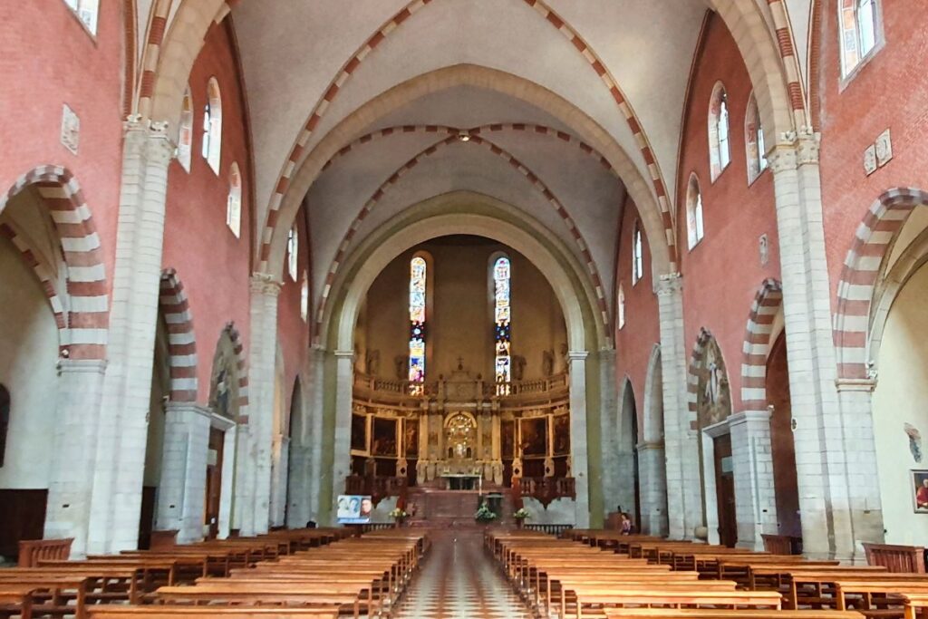 Blick durch das lange Hauptschiff der Kathedrale von Vicenza Richtung Altar. Zu sehen sind die hohen Gewölbedecken, die rötlich gefärbten Wände und die symmetrischen Säulenreihen.
