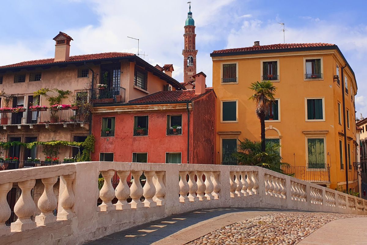 Die historische Steinbrücke Ponte San Michele in Vicenza überspannt den Fluss Retrone, im Hintergrund bunte Häuser und der Turm der Basilica Palladiana.