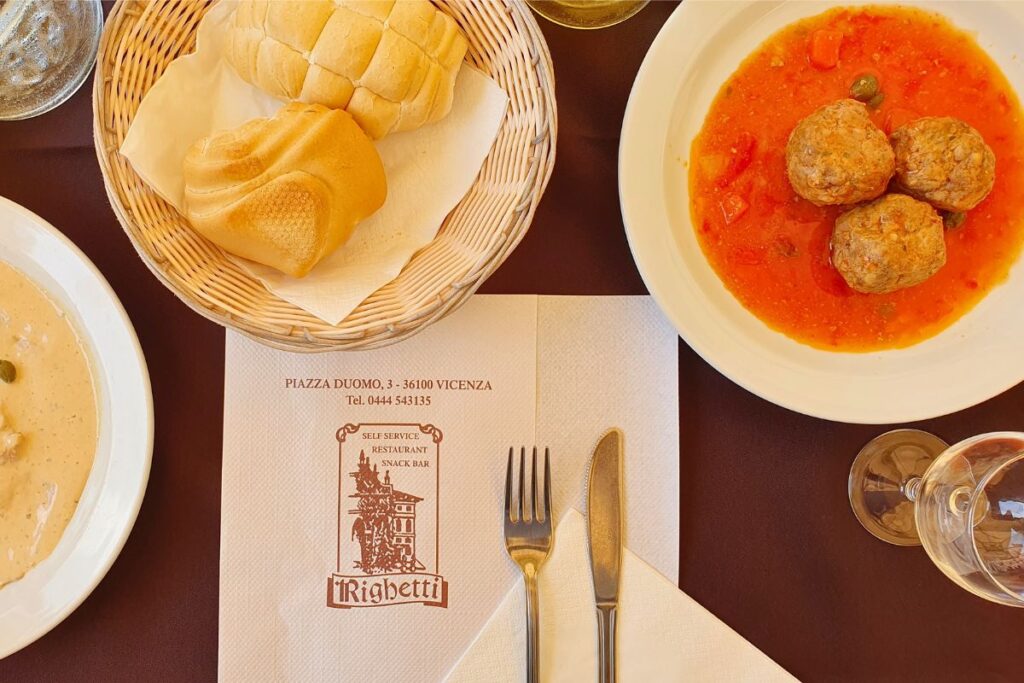 Draufsicht auf einen gedeckten Tisch im Restaurant Righetti in Vicenza mit Fleischbällchen in Tomatensauce, Brot und Wein.